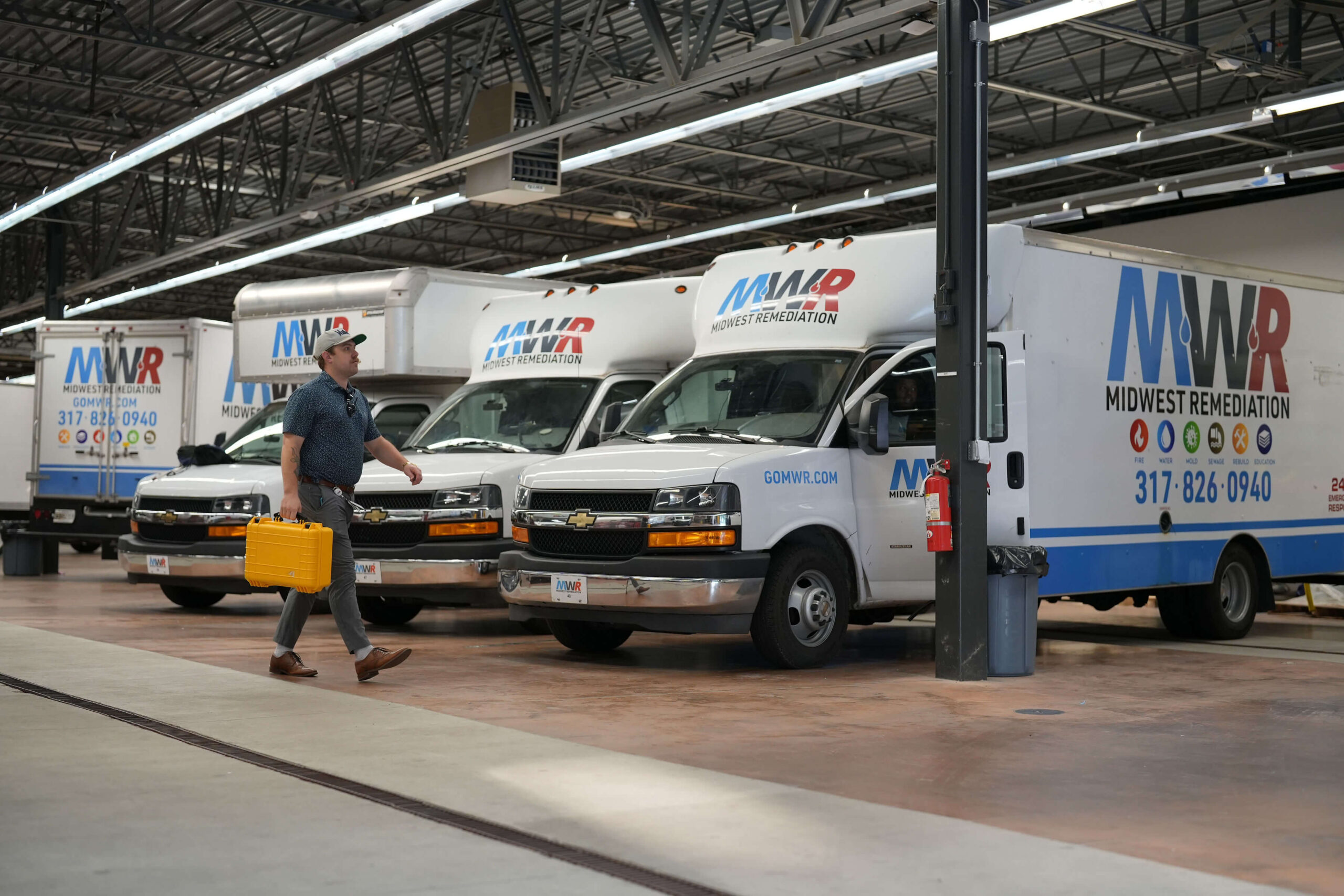 Midwest Remediation's trucks are lined up in a garage, while a man carrying a yellow briefcase walks next to them